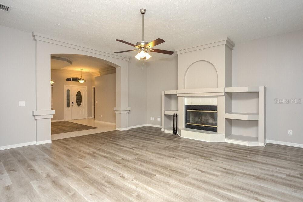 A living room features light wood-look flooring, a ceiling fan, and a built-in fireplace — 2304 GOLF MANOR BOULEVARD, VALRICO, FL