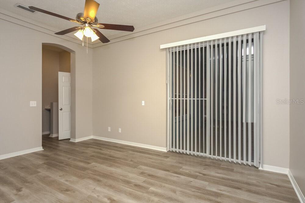 An empty room features wood-look flooring, a ceiling fan, and sliding glass patio doors — 2304 GOLF MANOR BOULEVARD, VALRICO, FL