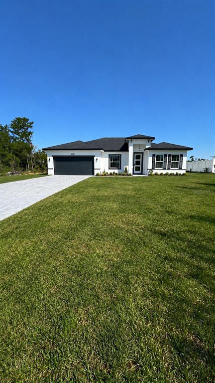 A single-story white house with a dark roof and garage sits on a grassy lot — 2487 SW 167TH LOOP, OCALA, FL