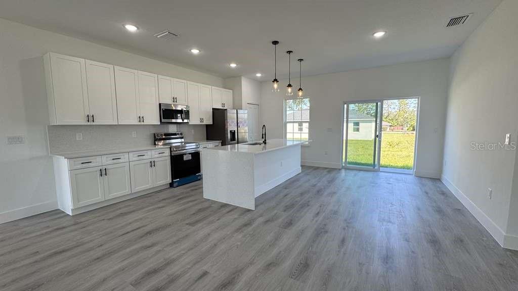A modern kitchen features white cabinetry, a central island, and light wood-look flooring — 2487 SW 167TH LOOP, OCALA, FL