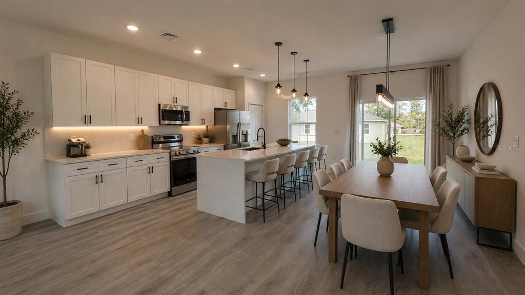 A modern kitchen and dining area with white cabinetry, a center island, and wood flooring — 2487 SW 167TH LOOP, OCALA, FL