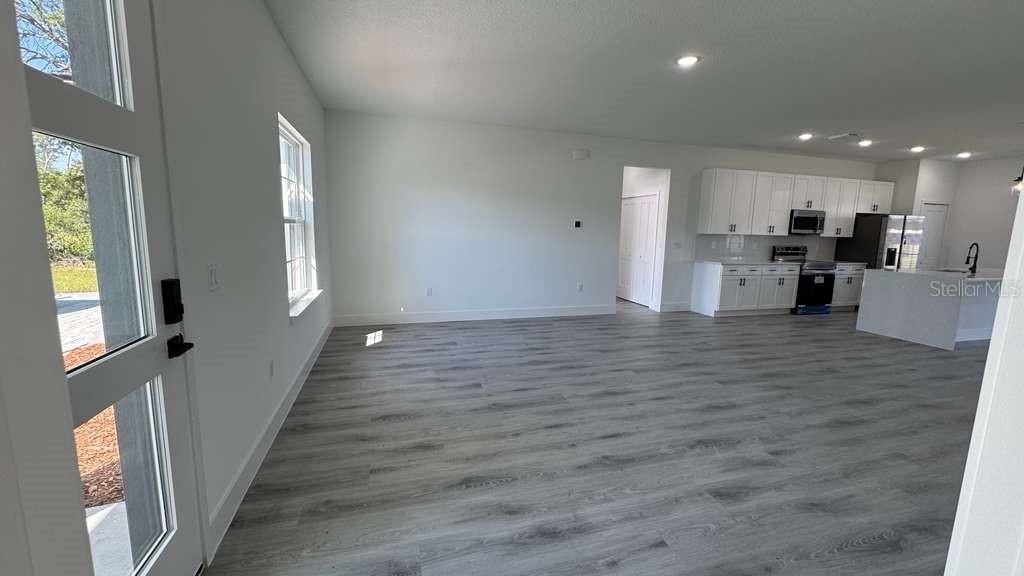 An open-concept living area features light gray wood-look flooring and a white kitchen with appliances — 2487 SW 167TH LOOP, OCALA, FL