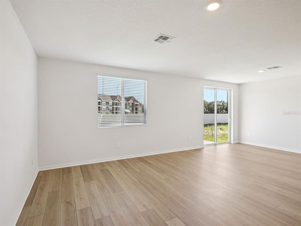 An empty room with light wood-look flooring, white walls, a window, and a sliding door — 10425 ABUNDANCE GROVE WAY, PARRISH, FL