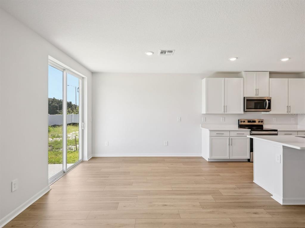 A bright kitchen and dining area features white cabinets, light wood flooring, and sliding glass doors — 10425 ABUNDANCE GROVE WAY, PARRISH, FL