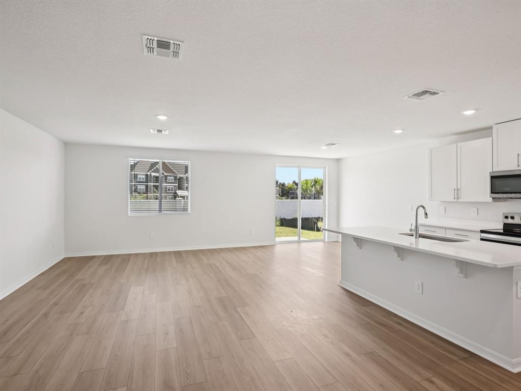 An open-concept living area features light wood-look flooring, white walls, and a modern kitchen — 10425 ABUNDANCE GROVE WAY, PARRISH, FL