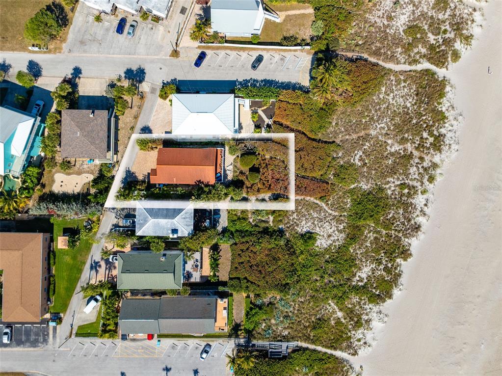 An aerial view shows a house with a red roof situated near a sandy beach — 8108 PRESIDENTIAL COURT, CAPE CANAVERAL, FL