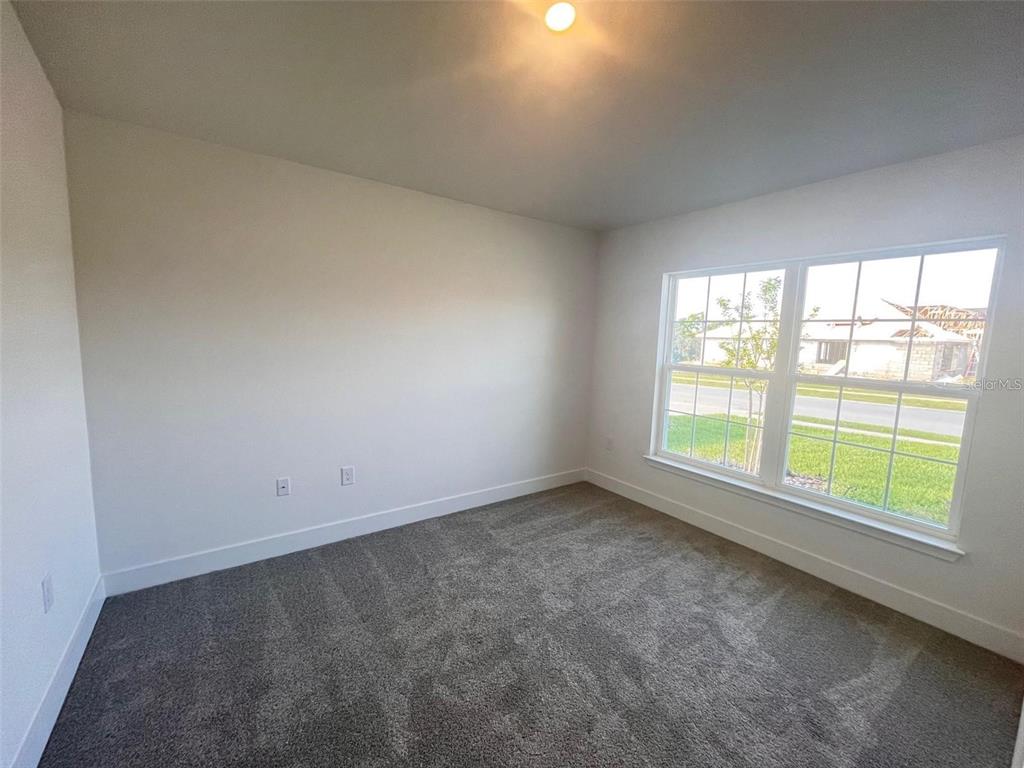 An empty bedroom features gray carpet, white walls, and a large window with exterior views — 13022 KENT BRADELY STREET, DADE CITY, FL