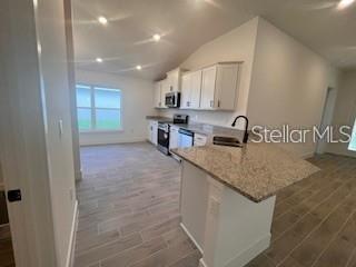 A kitchen features white cabinets, granite countertops, a center island, and light-colored wood-look tile flooring — 13022 KENT BRADELY STREET, DADE CITY, FL