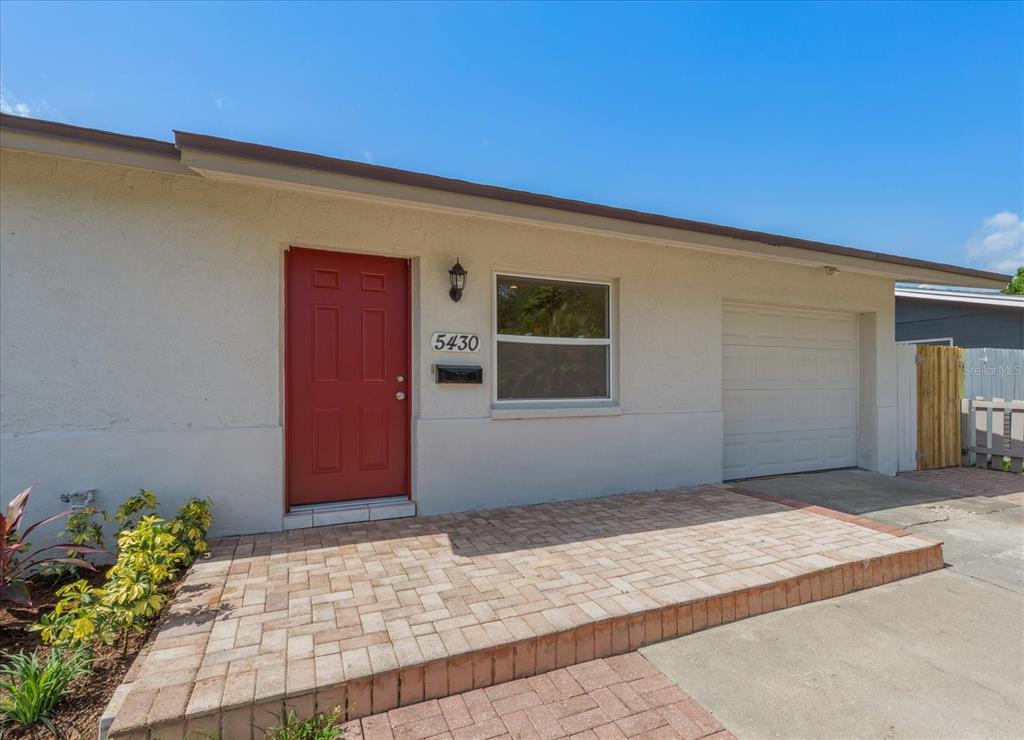 A single-story house exterior features a red front door, a brick patio, and a garage — 5430 98TH AVENUE N, PINELLAS PARK, FL