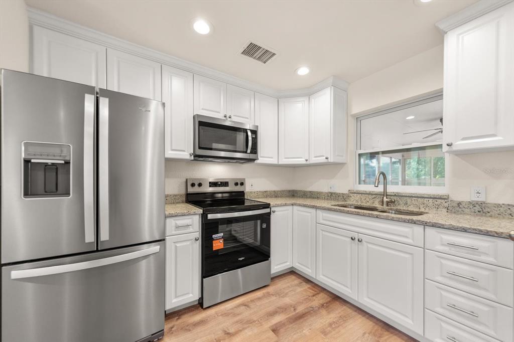 A kitchen features white cabinets, stainless steel appliances, granite countertops, and wood-look flooring — 5430 98TH AVENUE N, PINELLAS PARK, FL