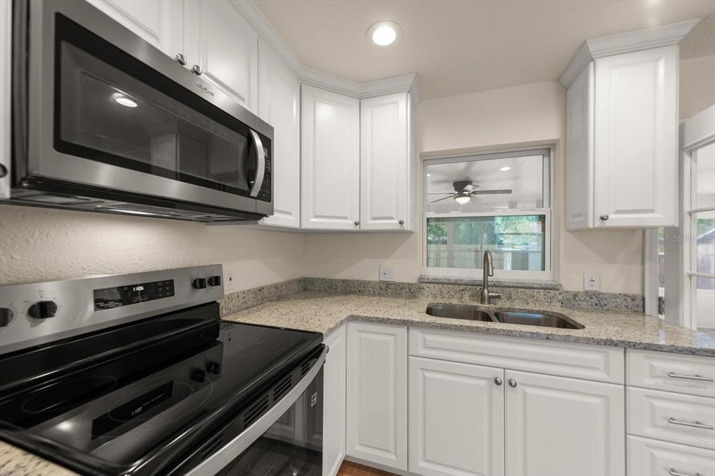 A kitchen features white cabinets, granite countertops, stainless steel appliances, and a double-basin sink — 5430 98TH AVENUE N, PINELLAS PARK, FL