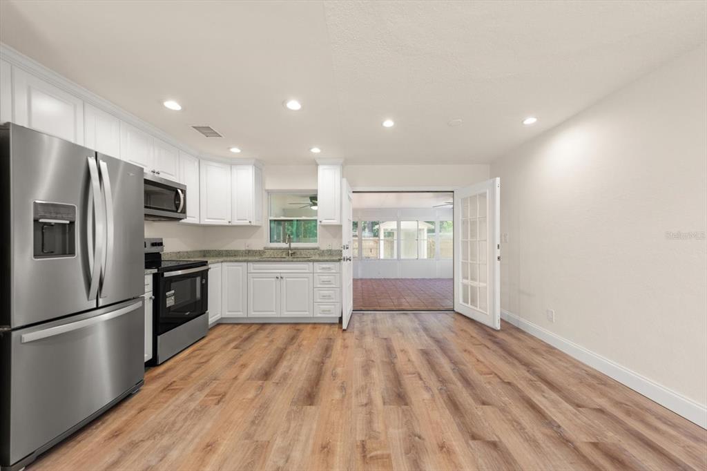 A kitchen with white cabinets, stainless steel appliances, and wood-look flooring opens to a patio — 5430 98TH AVENUE N, PINELLAS PARK, FL