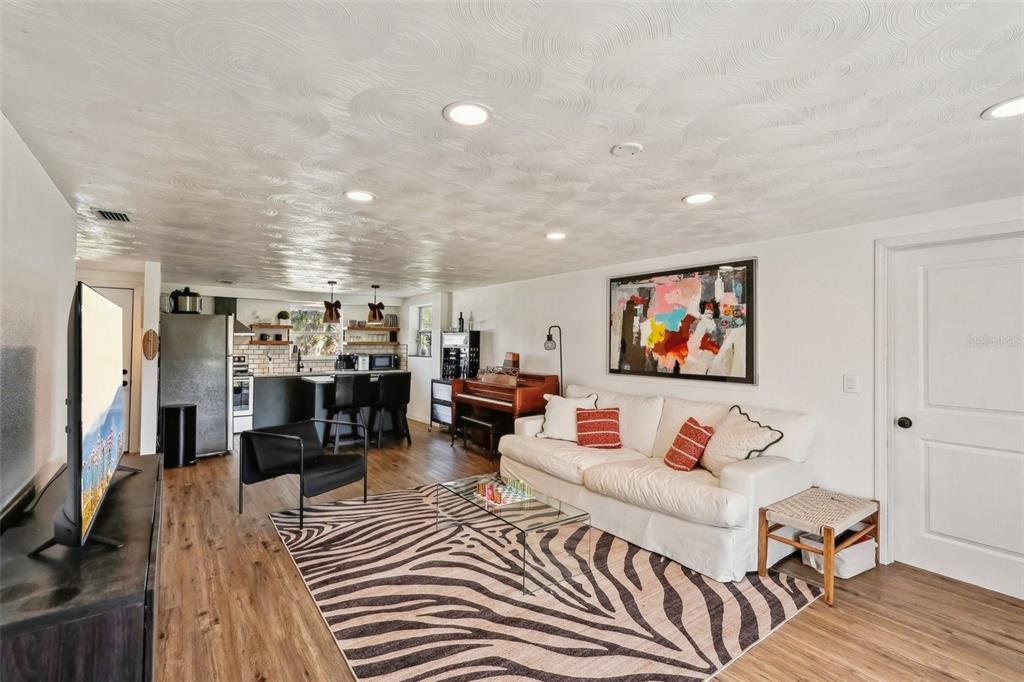 A living room with a zebra-print rug, white sofa, piano, and an open kitchen area — 107 TEMPLE ROAD, VENICE, FL