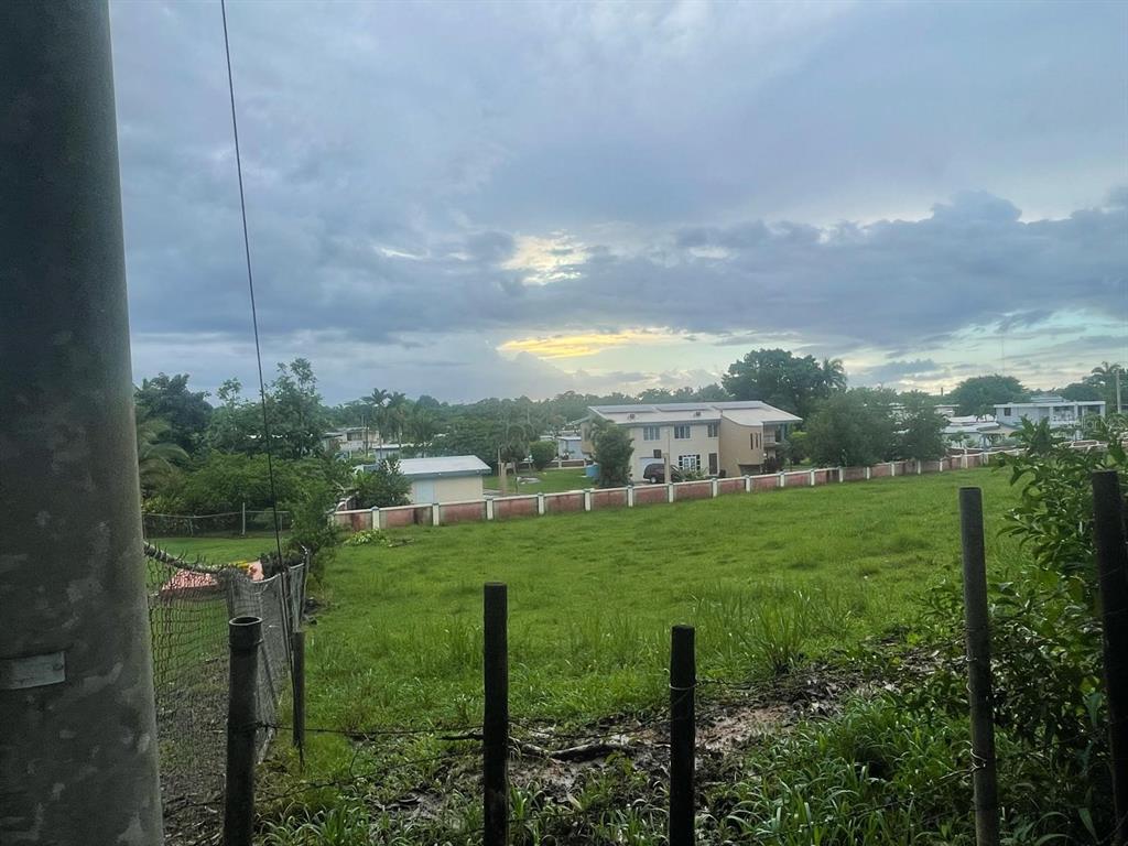A grassy lot sits in front of a residential neighborhood under a cloudy sky — PR-417 BARRIO MARIAS EN AGUADA, AGUADA, PR