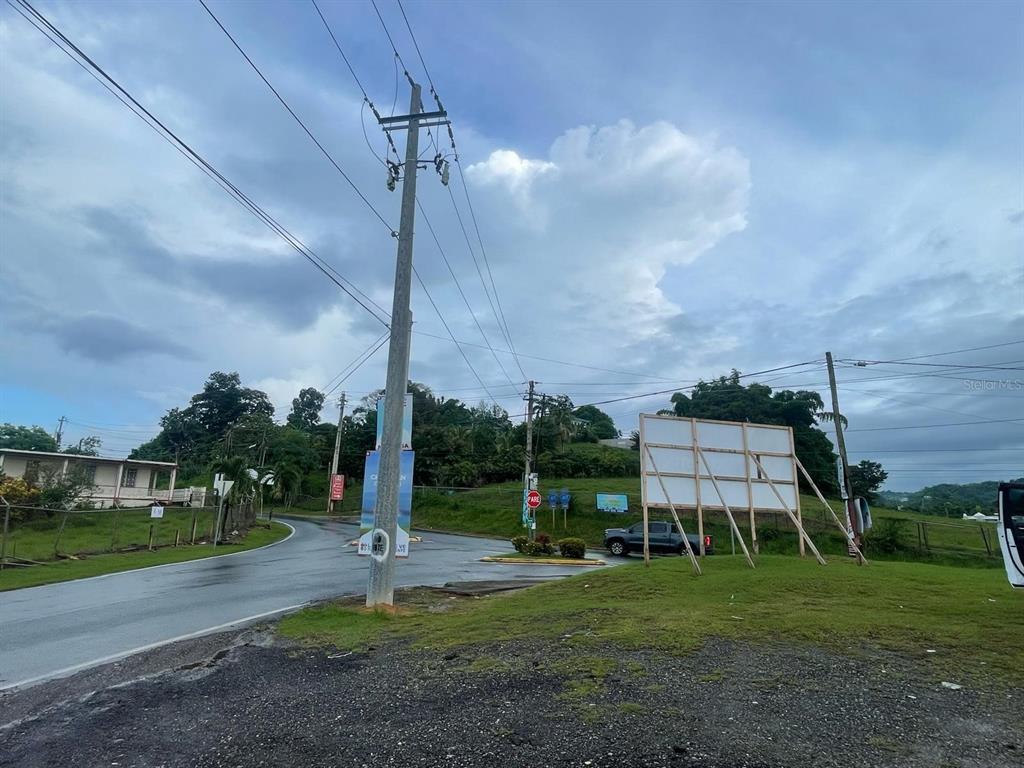 A paved road intersection features a utility pole, a large billboard, and a parked truck — PR-417 BARRIO MARIAS EN AGUADA, AGUADA, PR