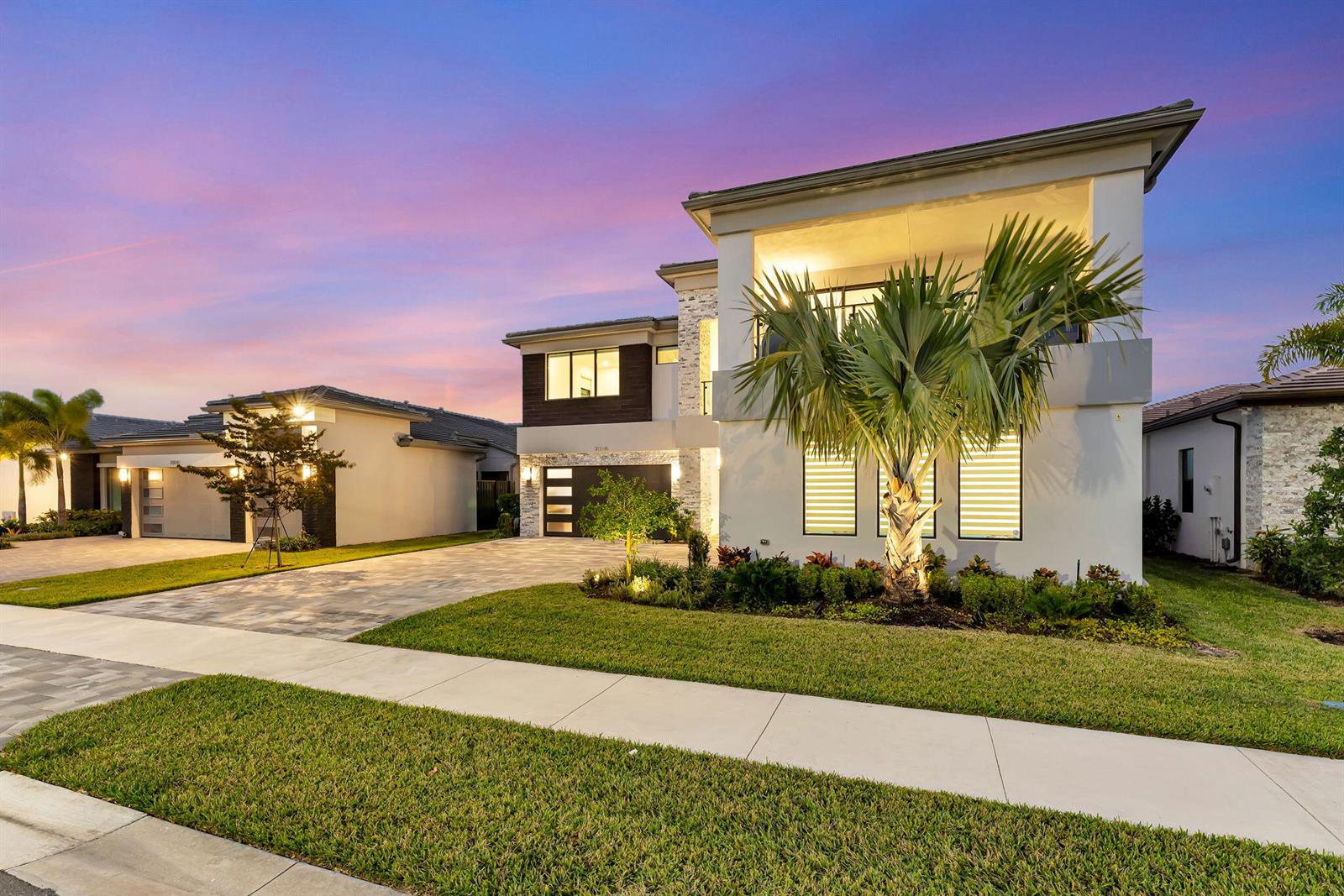 A modern two-story house with a paved driveway, palm tree, and stone accents at dusk — 20046 Pacific Dunes Drive, Boca Raton FL 33434, BOCA RATON, FL