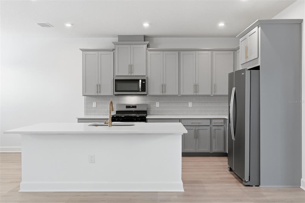 A modern kitchen features gray cabinets, a white island, and stainless steel appliances — 1859 SEAWALL WAY, CELEBRATION, FL