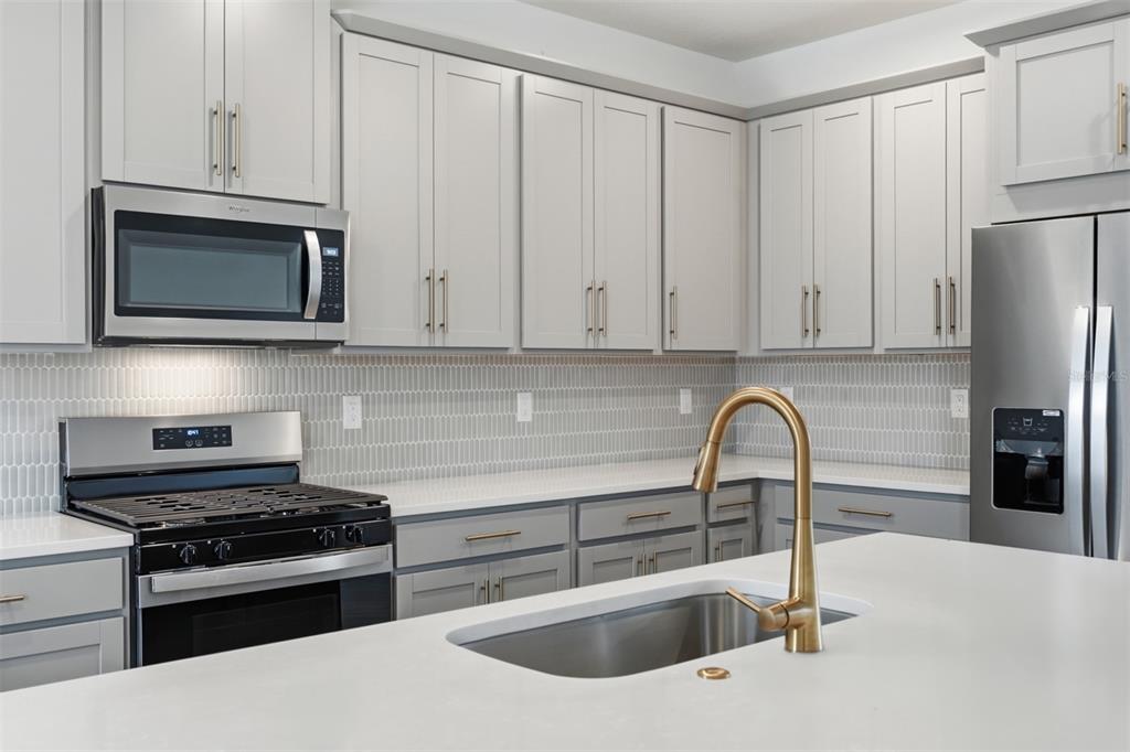 A kitchen features light gray cabinets, white countertops, a stainless steel stove, and gold fixtures — 1859 SEAWALL WAY, CELEBRATION, FL
