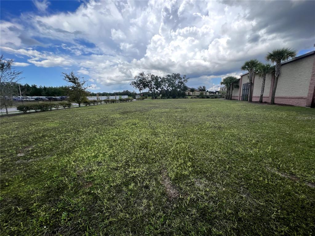 A large, grassy vacant lot sits next to a building with palm trees — 12249 CORTEZ BOULEVARD, BROOKSVILLE, FL