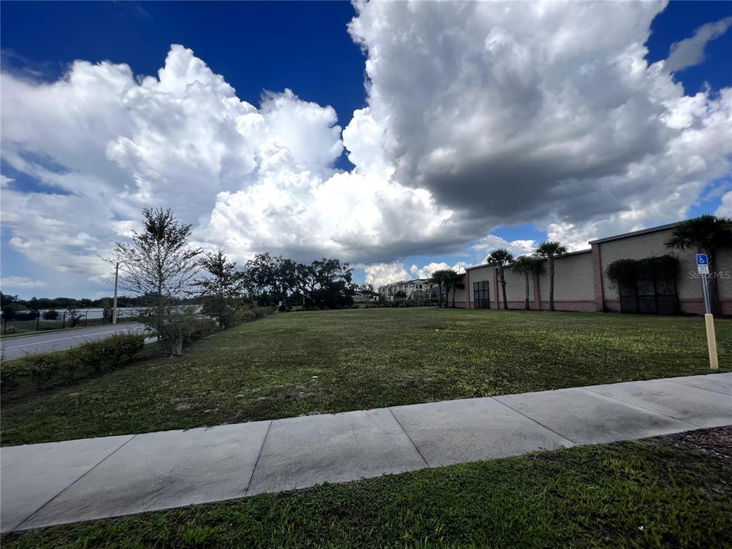 A vacant grassy lot sits next to a commercial building under a cloudy blue sky — 12249 CORTEZ BOULEVARD, BROOKSVILLE, FL