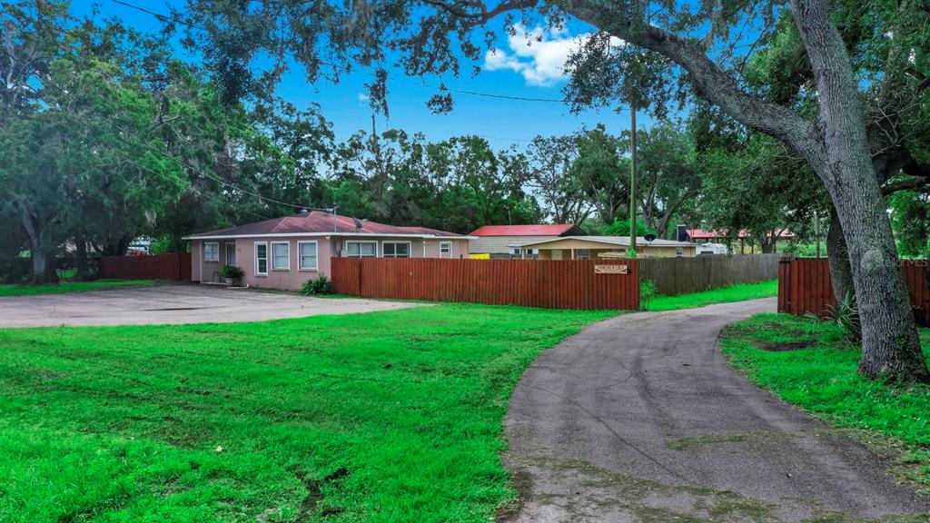 A single-story house with a fenced yard and a paved driveway under large trees — 6003 16TH AVENUE S, TAMPA, FL