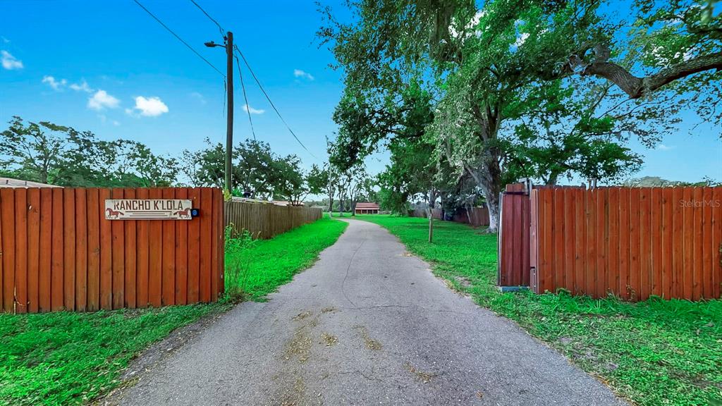 A paved driveway leads through a wooden gate toward a house on a grassy lot — 6003 16TH AVENUE S, TAMPA, FL