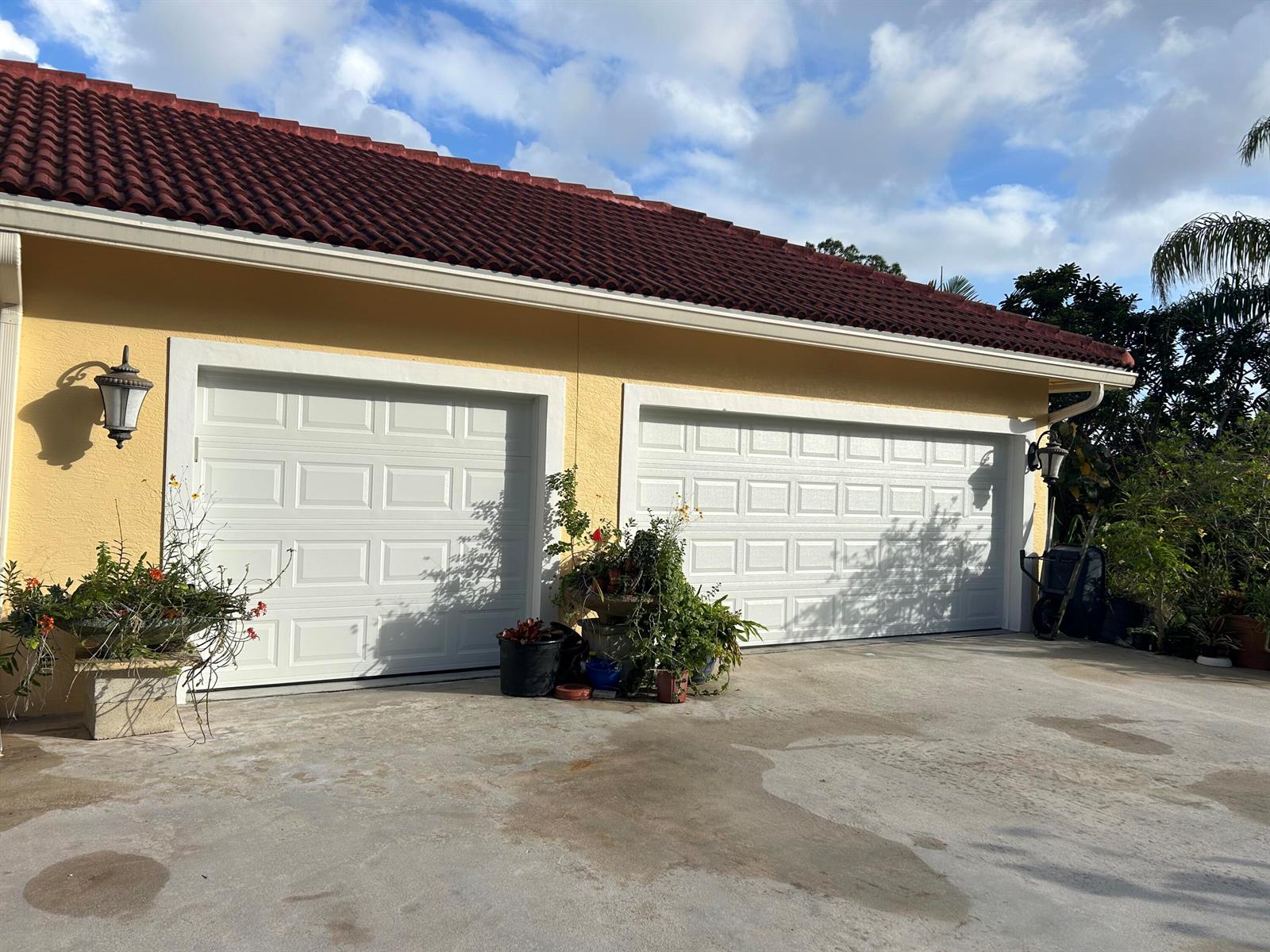 A yellow house exterior features two white garage doors, a red tile roof, and potted plants — 6220 Kelty Way, Lake Worth FL 33467, LAKE WORTH, FL