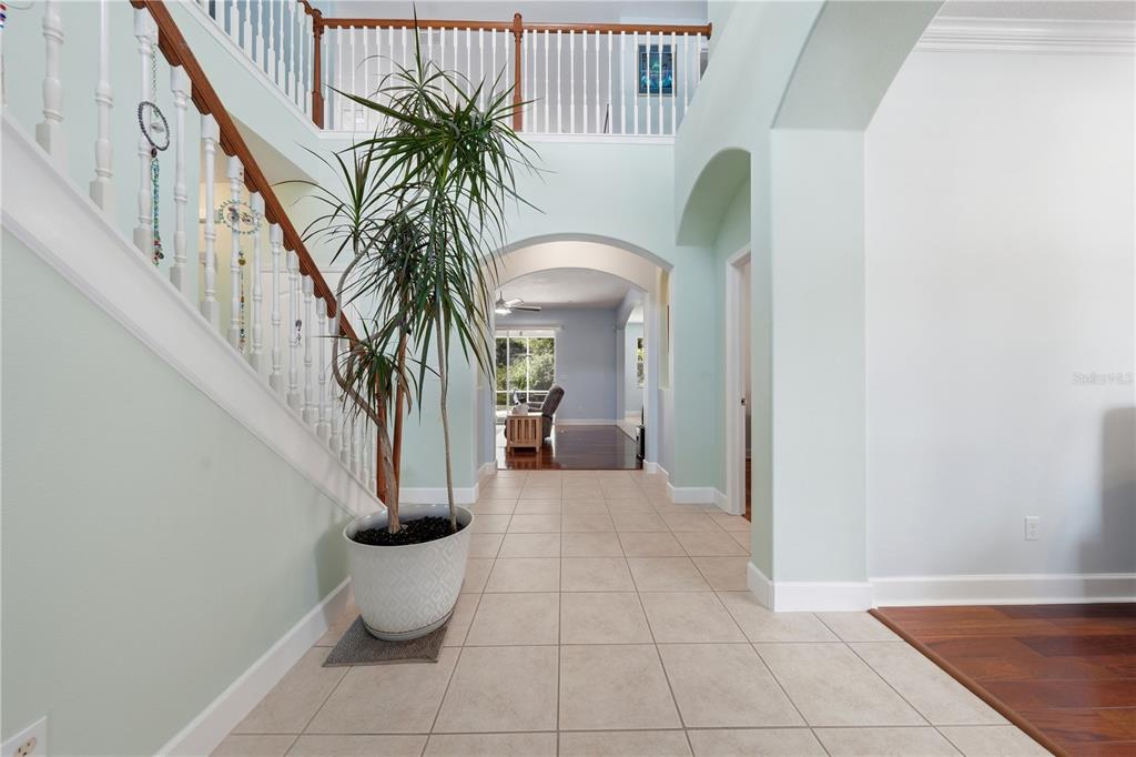 A tiled entryway features a staircase with a wooden railing and a large potted plant — 489 LUNA BELLA LANE, NEW SMYRNA BEACH, FL