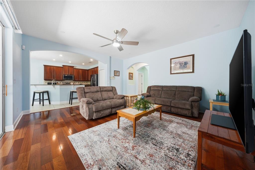 A living room with wood floors, two brown sofas, and an open kitchen in the background — 489 LUNA BELLA LANE, NEW SMYRNA BEACH, FL
