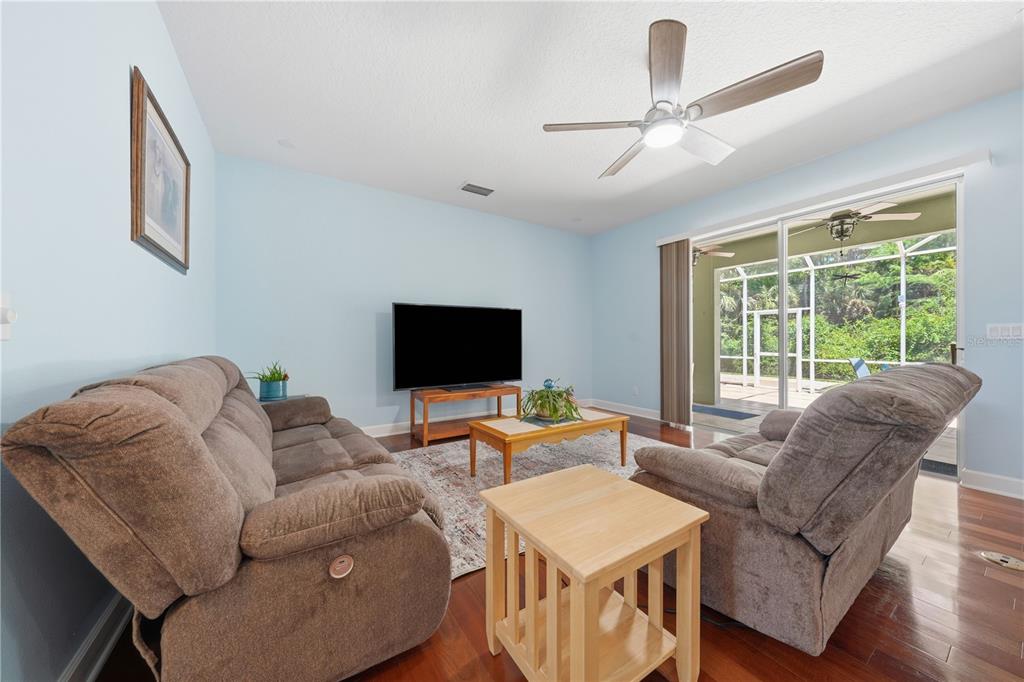 A living room with light blue walls, brown reclining furniture, and a sliding glass door — 489 LUNA BELLA LANE, NEW SMYRNA BEACH, FL
