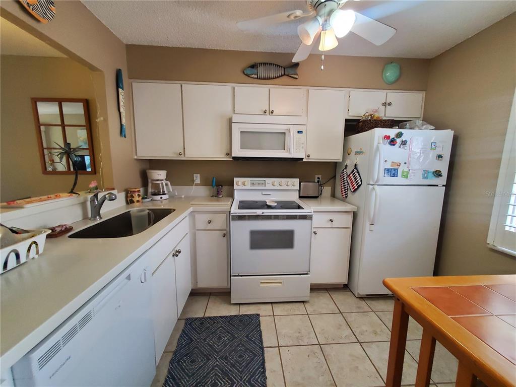 A kitchen features white cabinets, white appliances, tiled flooring, and a ceiling fan — 1400 ARROWHEAD CIRCLE W, CLEARWATER, FL