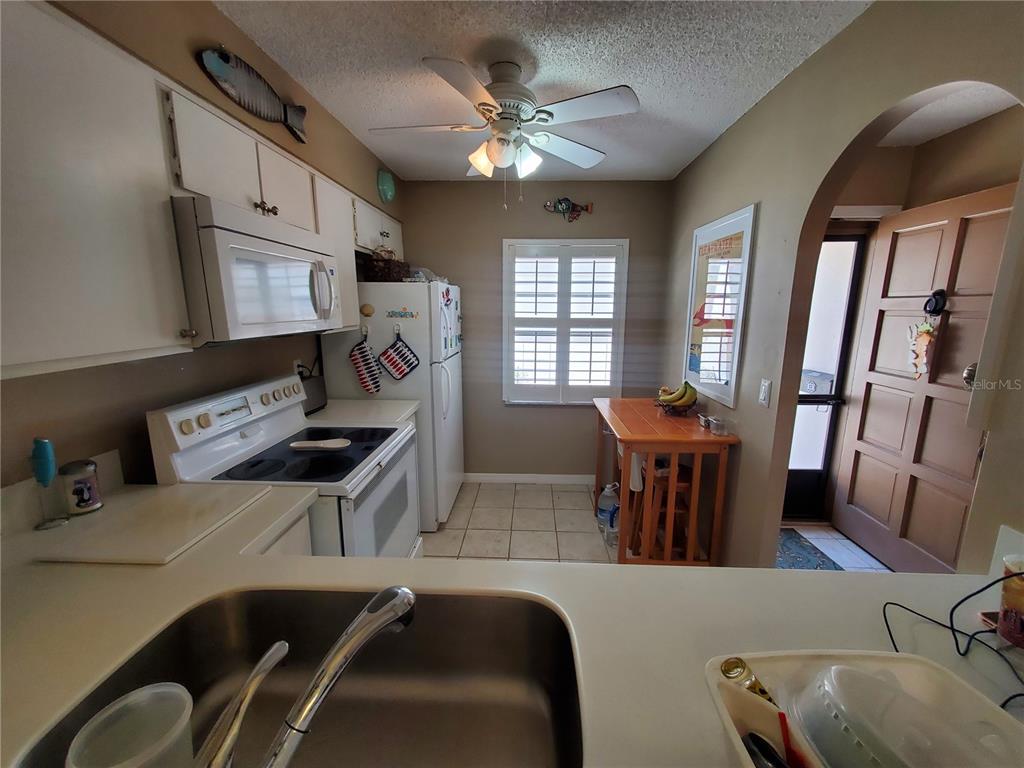 A kitchen features white cabinets, a white stove, a refrigerator, and a small wooden table — 1400 ARROWHEAD CIRCLE W, CLEARWATER, FL