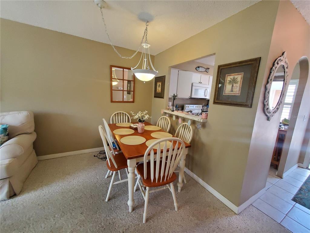 A dining area with a wooden table, white chairs, and a pass-through to the kitchen — 1400 ARROWHEAD CIRCLE W, CLEARWATER, FL