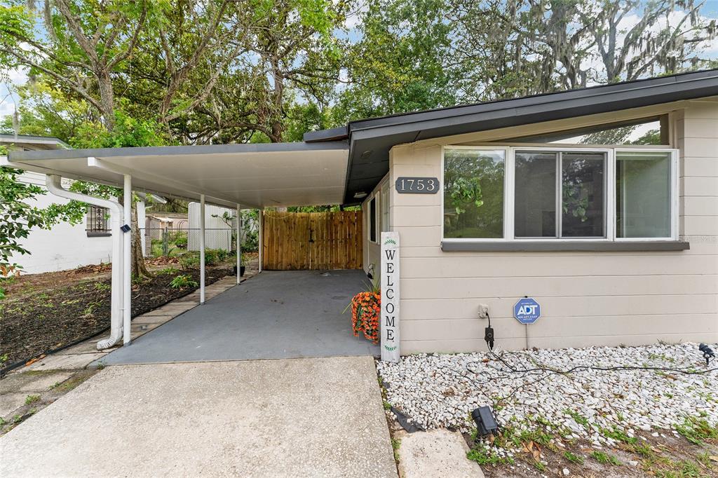 A house exterior features a concrete carport, a welcome sign, and a large front window — 1753 NE 20TH PLACE, GAINESVILLE, FL