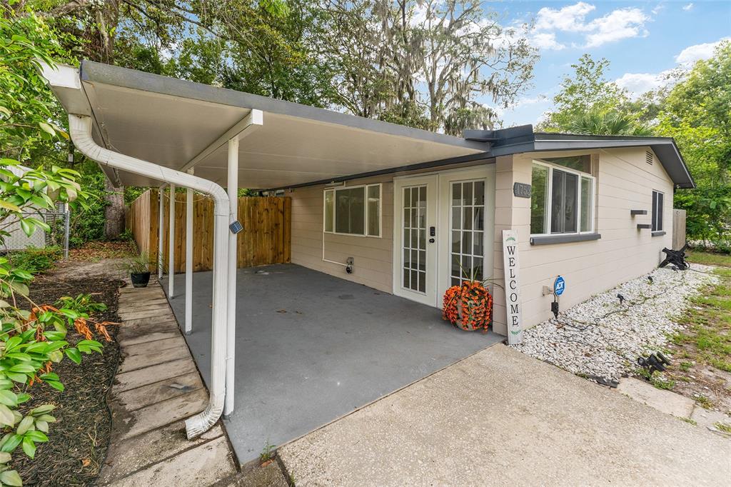 A beige house exterior features a covered carport, white-framed glass doors, and a gravel yard — 1753 NE 20TH PLACE, GAINESVILLE, FL