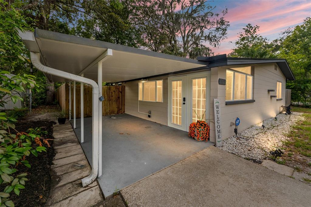 A single-story house exterior features a concrete carport, a white front door, and gravel landscaping — 1753 NE 20TH PLACE, GAINESVILLE, FL