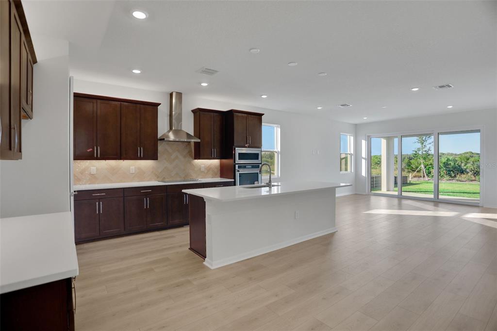 A modern kitchen with dark wood cabinets, white countertops, and an island overlooks a backyard — 13524 TURNLEAF BOULEVARD, PUNTA GORDA, FL