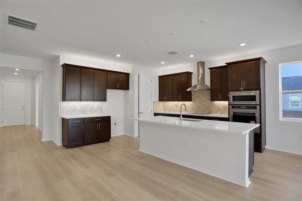 A modern kitchen features dark wood cabinets, white countertops, a central island, and light flooring — 13524 TURNLEAF BOULEVARD, PUNTA GORDA, FL