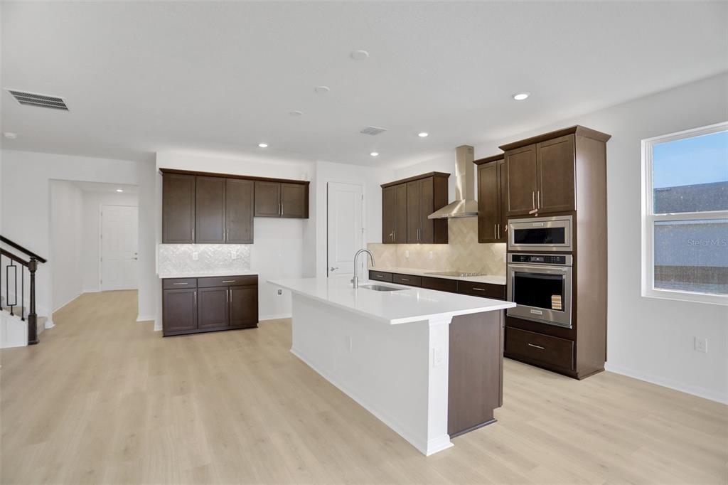 A modern kitchen features dark wood cabinets, white countertops, stainless steel appliances, and light flooring — 13524 TURNLEAF BOULEVARD, PUNTA GORDA, FL