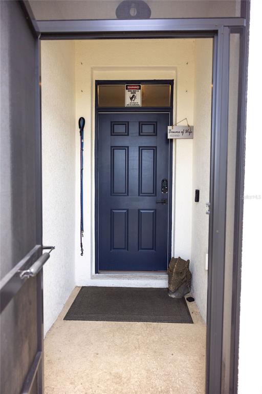 A dark blue front door with a dog leash and signs sits in a covered entryway — 3852 MOSSY LIMB COURT, PALMETTO, FL