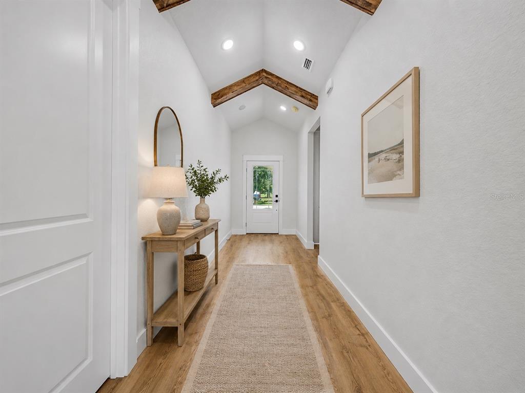 A hallway with a vaulted ceiling, exposed wood beams, wood flooring, and a console table — 7159 GOLF CLUB DRIVE, SEBRING, FL