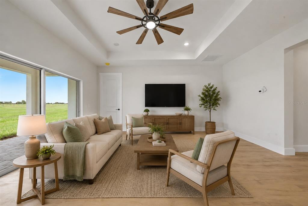 A bright living room features a tray ceiling, wood-look flooring, and a large sliding glass door — 7159 GOLF CLUB DRIVE, SEBRING, FL