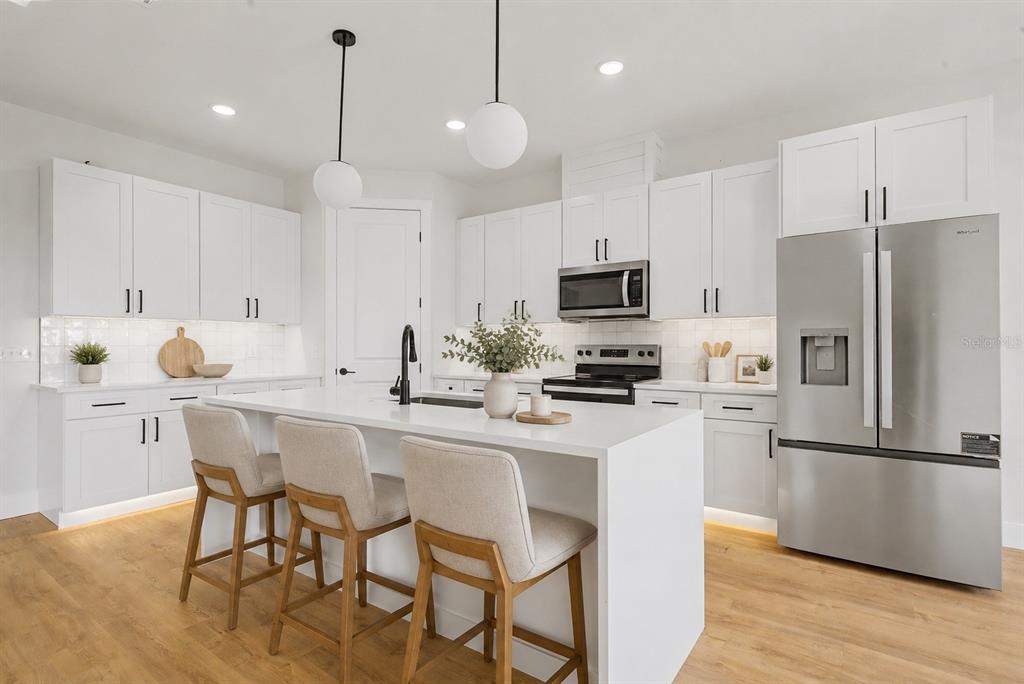 A modern kitchen features white cabinetry, a central island with bar seating, and stainless appliances — 7159 GOLF CLUB DRIVE, SEBRING, FL