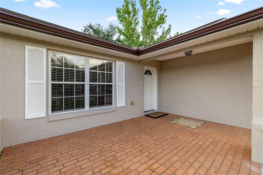A covered brick patio leads to a white front door beside a window with shutters — 36 ALMOND DRIVE, OCALA, FL