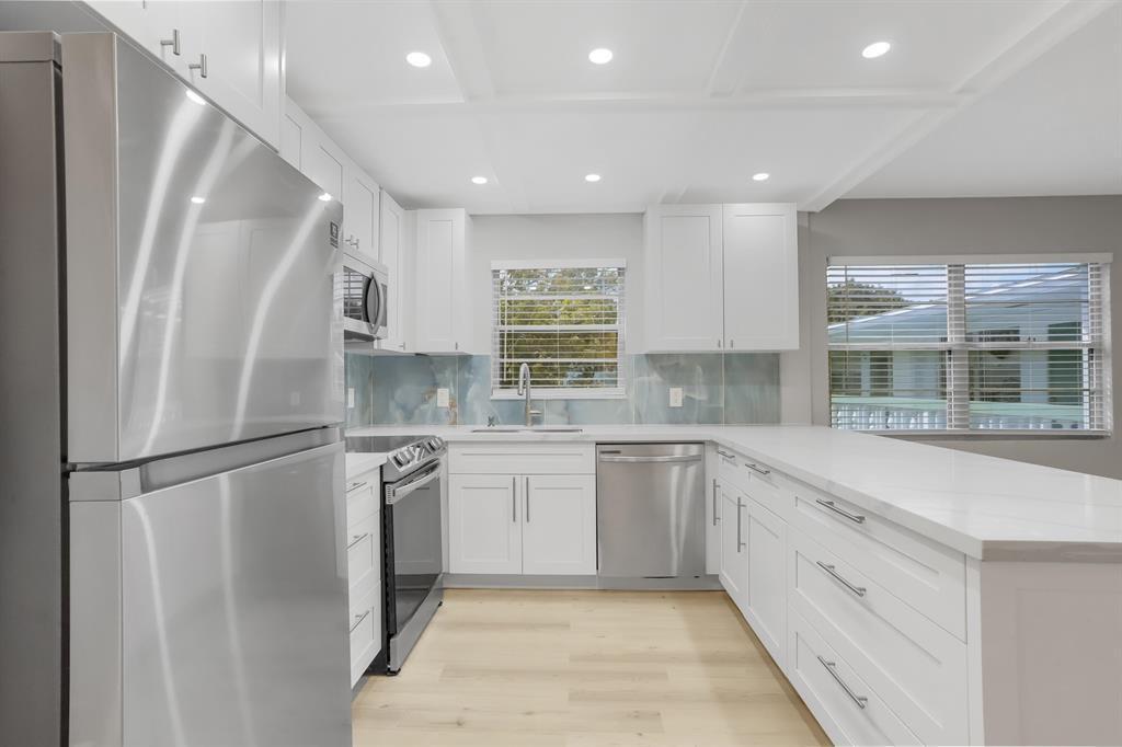 A modern kitchen features white cabinets, stainless steel appliances, quartz countertops, and a blue backsplash — 40 Prescott B # 40, Deerfield Beach FL 33442, DEERFIELD BEACH, FL