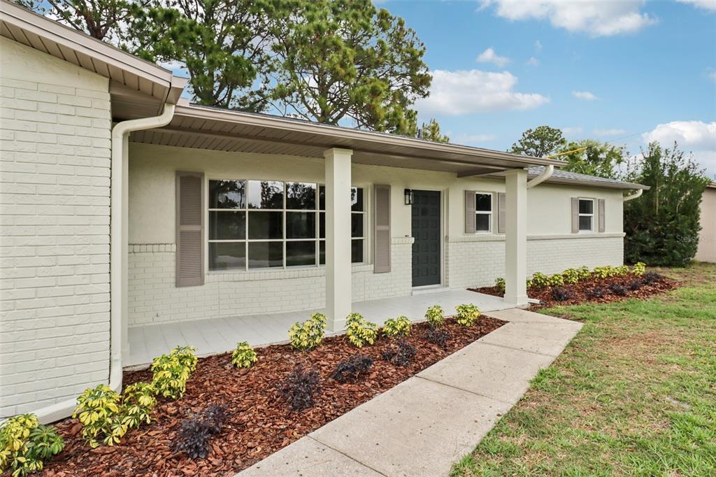 A single-story house with a white brick exterior, covered front porch, and landscaped front yard — 1412 DIGARMO TERRACE, DELTONA, FL