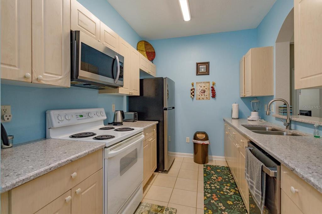 A galley kitchen features light wood cabinets, granite countertops, and stainless steel appliances — 2302 SILVER PALM DR UNIT 204, KISSIMMEE, FL