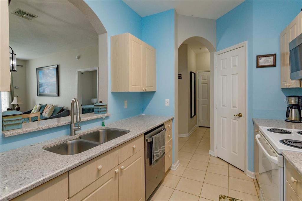 A kitchen features light wood cabinets, granite countertops, a double sink, and blue walls — 2302 SILVER PALM DR UNIT 204, KISSIMMEE, FL