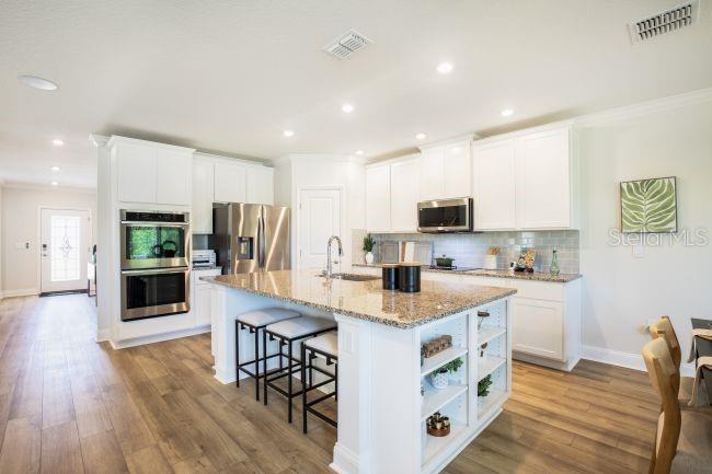 A kitchen features white cabinets, granite countertops, a large island with seating, and stainless appliances — 16817 NW 176TH WAY, ALACHUA, FL