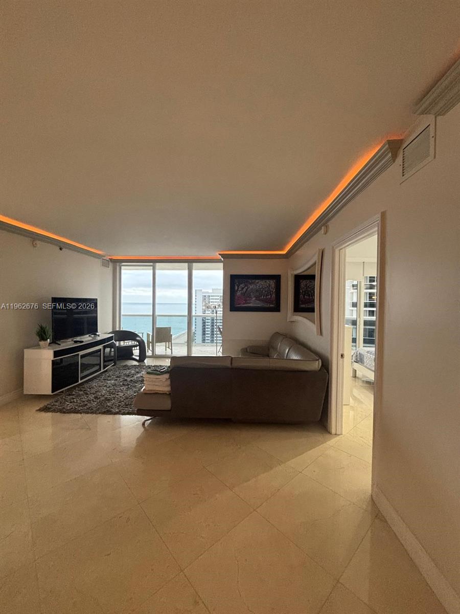 A living room with tile floors, a gray sectional sofa, and orange cove lighting — 1830 S OCEAN DR # 2004, Hallandale Beach FL 33009, HALLANDALE BEACH, FL